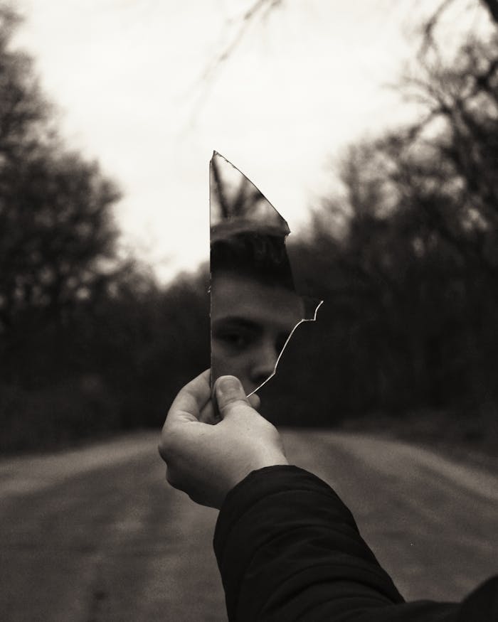 A thought-provoking black and white image of a man looking into a broken mirror.