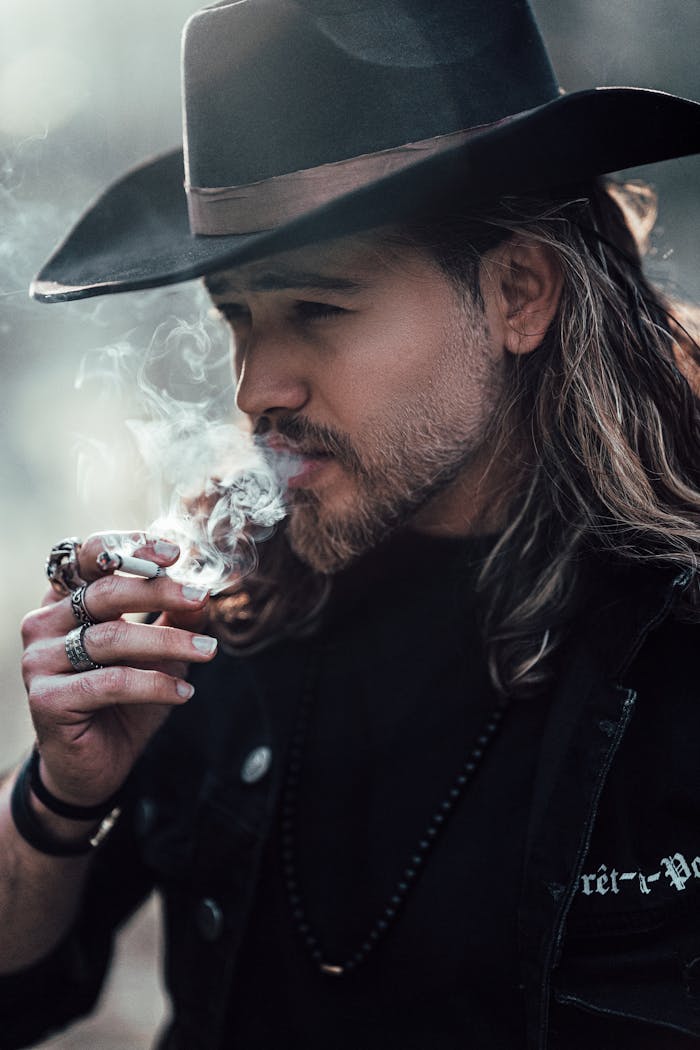 services-03 A man with a cowboy hat smoking, showcasing Western style and contemplation.