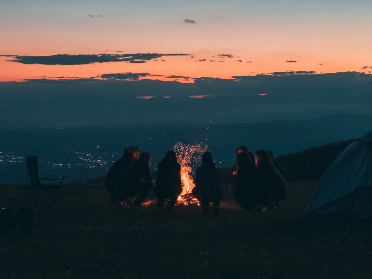 A group of people gathering around a campfire at dusk, enjoying the scenic view and warm firelight.