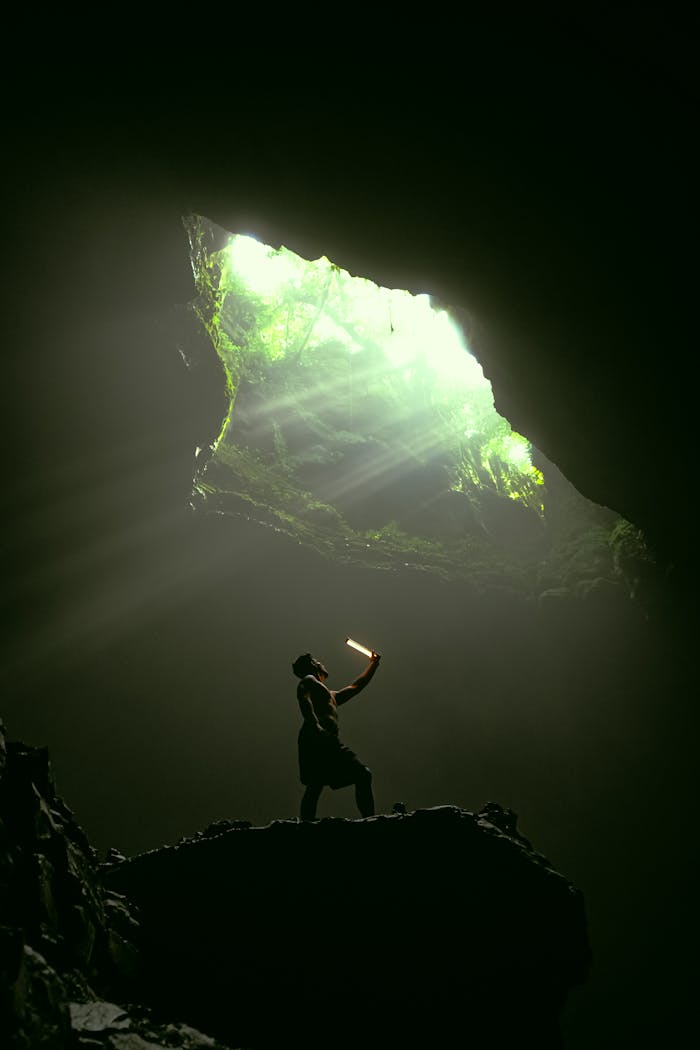 Silhouette of a climber in a cave illuminated by a sunlit opening.